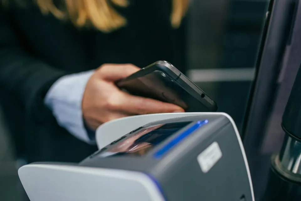 Mão segurando um celular para pagar por aproximação numa maquininha