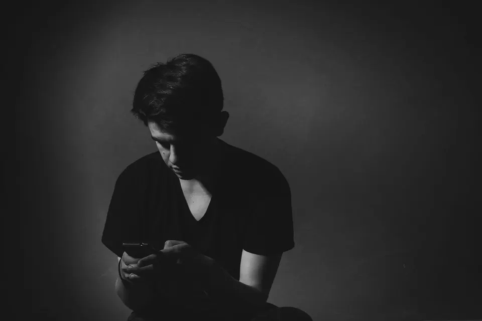 Jovem num quarto escuro olhando o celular, em preto e branco