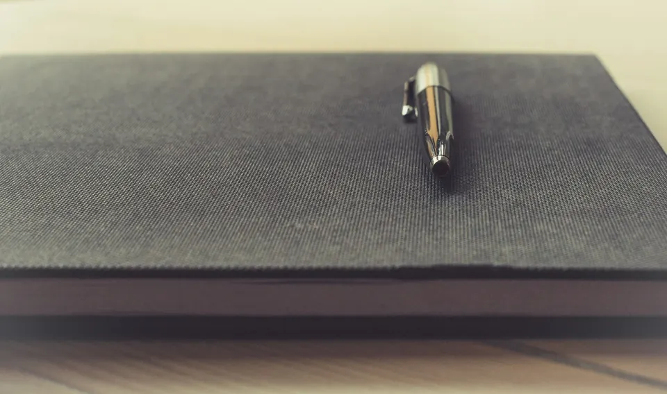 Caneta apoiada sobre um caderno cinza de capa texturizada
