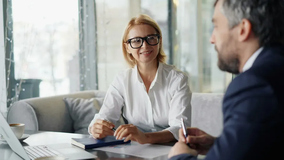 Um homem e uma mulher conversam sentados à mesa com um notebook
