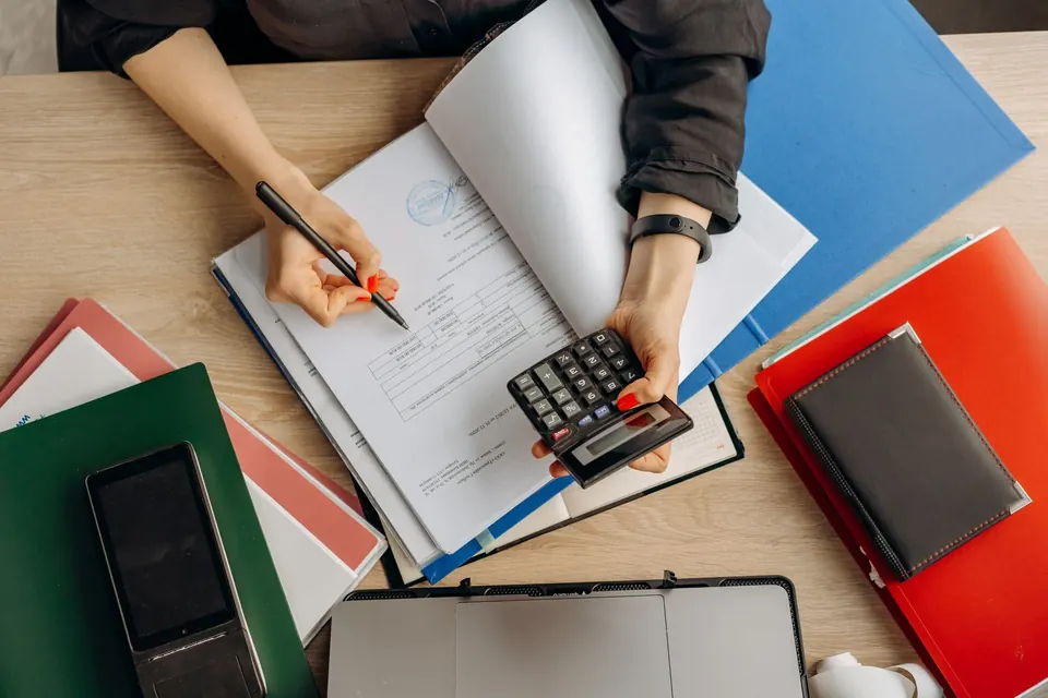 Pessoa analisa documentos com uma calculadora sobre a mesa